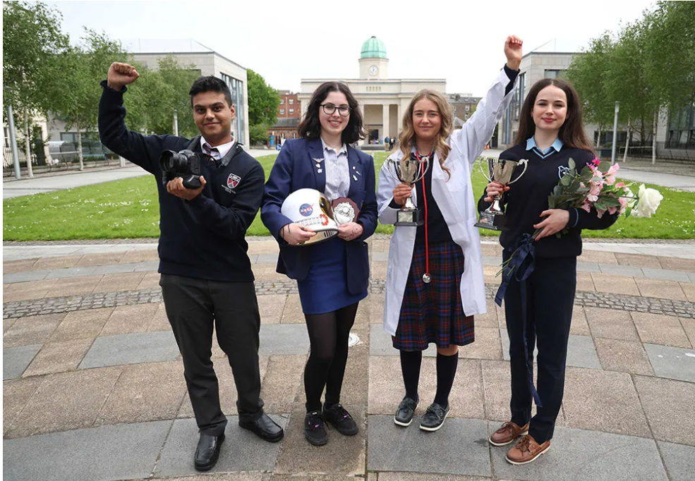 Four students holding trophies and a NASA helmet outside after the career skills competition.
