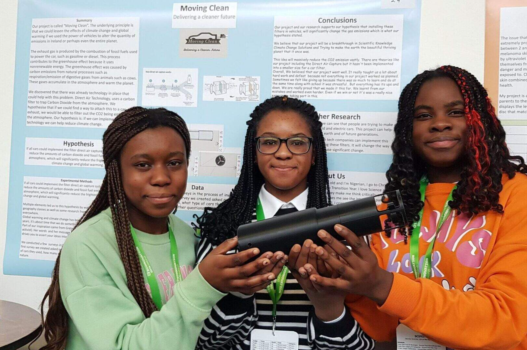 Three students holding their "Moving Clean" carbon-capture device in front of their project poster.