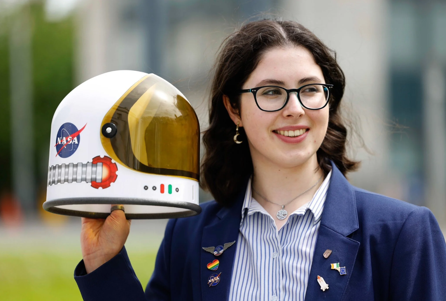 Portrait holding a NASA astronaut helmet, wearing a blazer with space-themed pins.